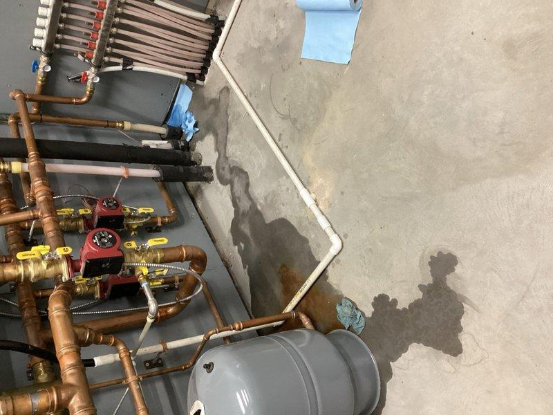 Completed preventive maintenance tune-up on HVAC equipment and hydronic heating system. Inspected boiler installation in mechanical room, documenting extensive copper piping network with multiple zone valves, expansion tank, and circulator pump assembly. Identified active leak in boiler system located in shed/shop area, evidenced by water staining on concrete floor beneath equipment. Photographed leak source and affected piping connections for estimate preparation and customer approval before proceeding with repairs.