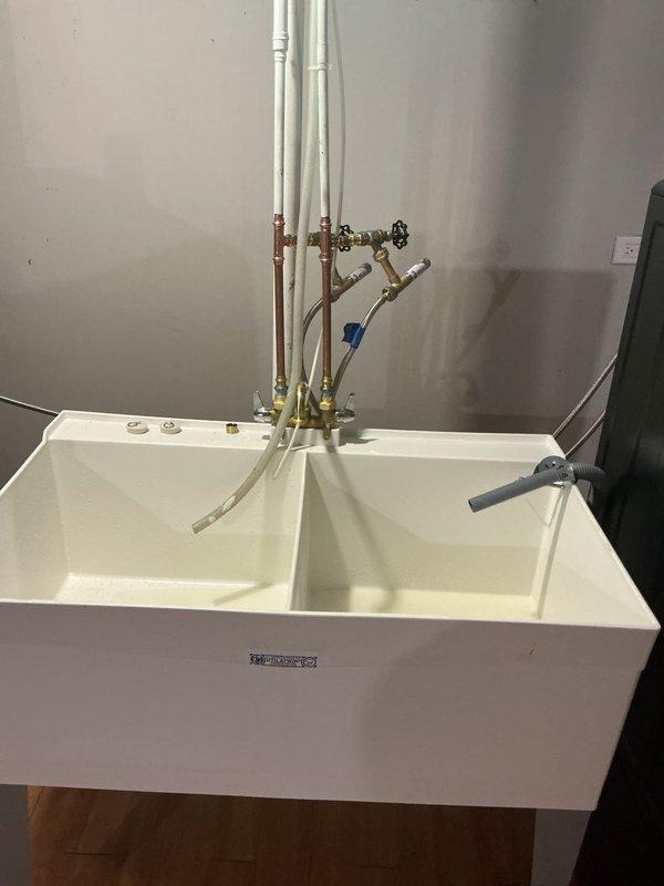 Installed a new white dual-compartment laundry tub with a two-handle faucet assembly, connecting to existing water supply lines and drain infrastructure. The installation included mounting the utility sink, connecting brass shut-off valves, attaching supply hoses to the faucet, and verifying proper drainage through the existing PVC P-trap assembly. All connections were tested and confirmed leak-free upon completion.