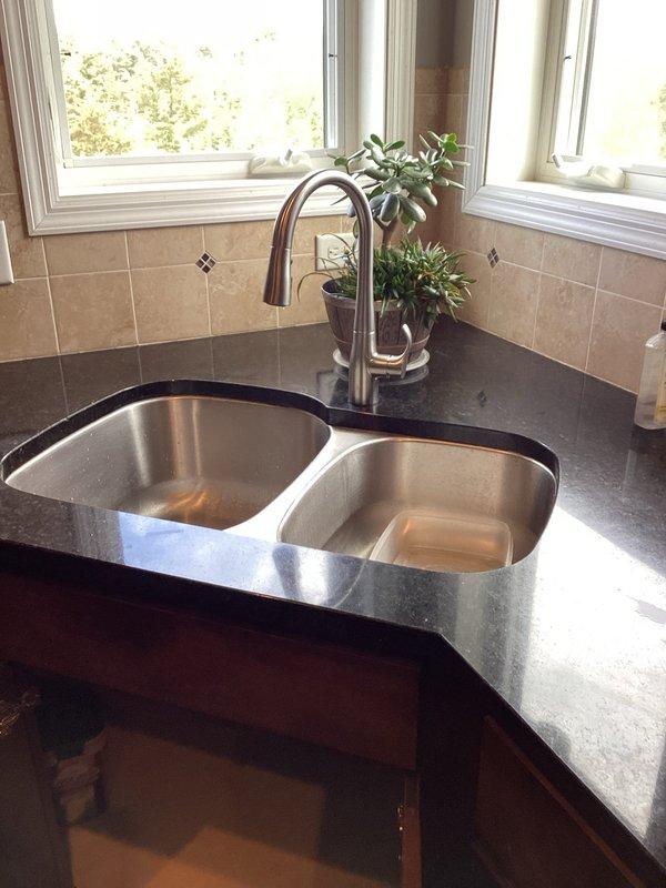 Responded to kitchen faucet leak caused by damaged sprayer hose. Upon inspection, determined that the hose leak warranted complete faucet replacement to ensure long-term reliability. Successfully removed existing faucet assembly and installed new pull-down kitchen faucet with bronze finish on double-basin stainless steel sink. Tested water flow and spray functions to verify proper operation with no leaks detected. System restored to full working condition.