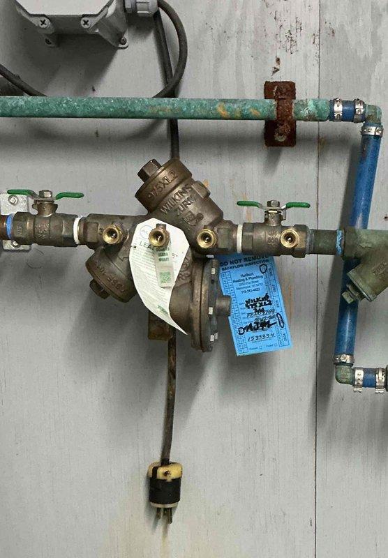 Responded to water leak at RPZ backflow preventer assembly located in parlor near chemical room. Upon inspection, identified active leak at Wilkins backflow prevention device and determined Y strainer requires replacement due to failure. Documented existing conditions showing corrosion on green supply pipe, aged brass valve assembly with compliance tags intact, and multiple ball valves in system. Ordered necessary replacement parts for Y strainer to complete repair and restore proper operation of backflow prevention system.