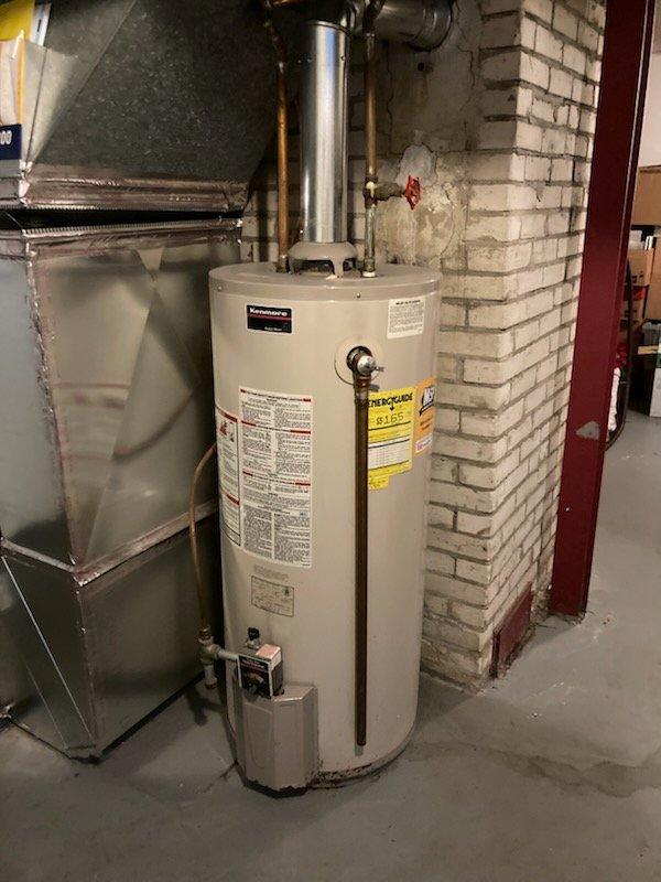 Responded to service call for 23-year-old conventional tank water heater experiencing leak from bottom of unit. Upon inspection, confirmed active water seepage at base of Kenmore Power Miser tank-style water heater in basement utility area. Due to age of unit and location of leak, determined tank failure requiring full replacement rather than repair. Coordinated replacement installation, shut off water supply and gas connections, drained existing unit, and removed failed water heater from service area. Prepared site for new equipment installation with proper clearances and access to existing copper supply lines, gas piping, and venting infrastructure.