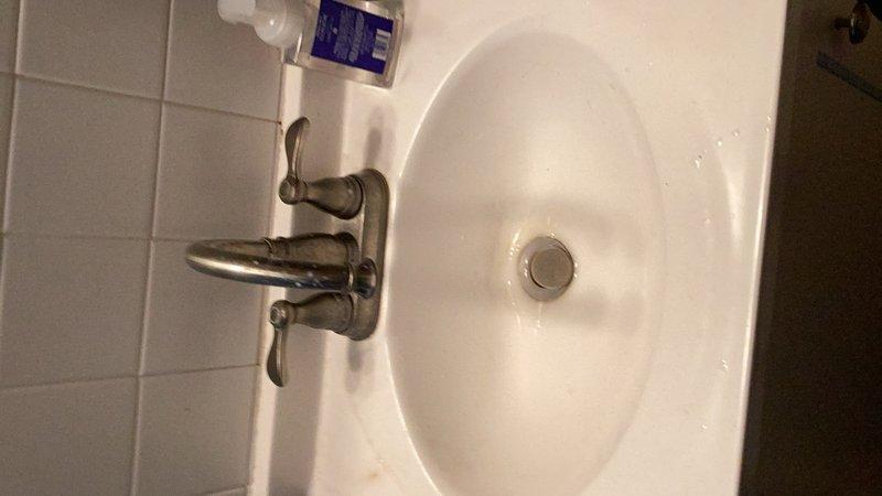 Completed comprehensive plumbing inspection of residential property, examining all accessible fixtures and systems. Inspected bathroom sink with dual-handle faucet assembly, drain stopper mechanism, and surrounding plumbing connections, confirming proper operation and no visible leaks. Documented electrical panel and exposed plumbing infrastructure in unfinished area for reference.