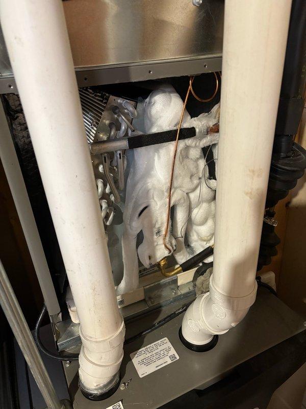 Responded to no cooling condition on 1-year-old system experiencing repeat evaporator coil freeze-up. Upon arrival, found evaporator coil completely encased in ice with frost extending along suction line to outdoor compressor unit. Detected refrigerant leaks within indoor unit but unable to perform comprehensive leak detection due to extensive ice accumulation on coil assembly. Documented frozen coil condition and suction line with photographs showing heavy frost buildup on refrigerant lines in crawlspace and complete ice encasement of evaporator coil within air handler cabinet. System requires follow-up visit after coil thaw to conduct thorough leak detection and determine if failure is related to thermostatic expansion valve malfunction or evaporator coil leak.