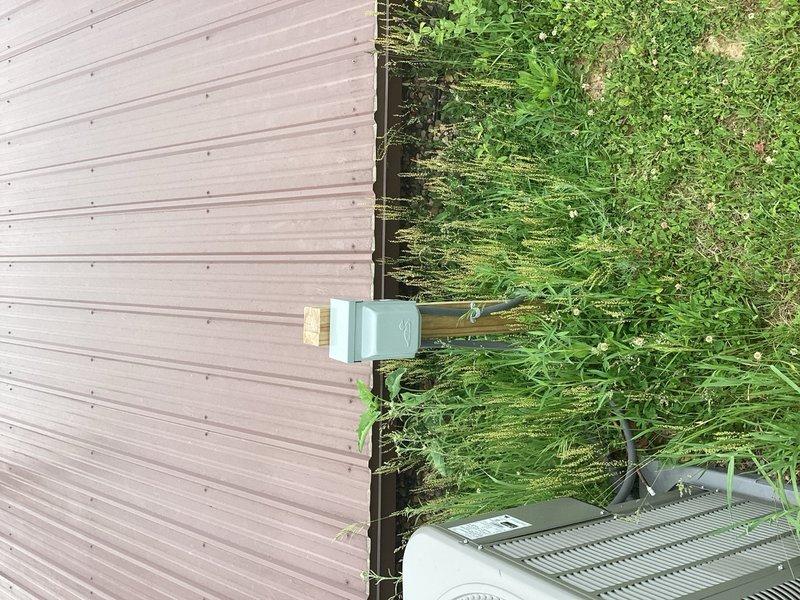 Provided estimate for new outdoor hose bib installation near AC unit. Scope includes upgrading existing water line to 3/4" supply, routing through attic space, and penetrating exterior wall adjacent to condenser location. Installation will include dedicated shut-off valve in mechanical room above water main and boiler drain for seasonal winterization to prevent freeze damage. Exterior hose bib will be mounted to post similar to existing AC disconnect switch configuration. Documented site conditions and existing infrastructure with photographs for accurate material specifications and labor requirements.