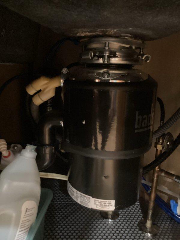 Responded to service call for non-functioning garbage disposal that was initially making a buzzing noise before ceasing all operation. Upon inspection, used allen wrench to manually rotate the disposal mechanism to check for jammed impeller. Reset the disposal unit using the reset button located on the bottom of the unit. Assessed disposal functionality and determined unit was operational after reset procedure. Documented equipment condition with photographs showing InSinkErator disposal unit installation under sink and drain opening condition.