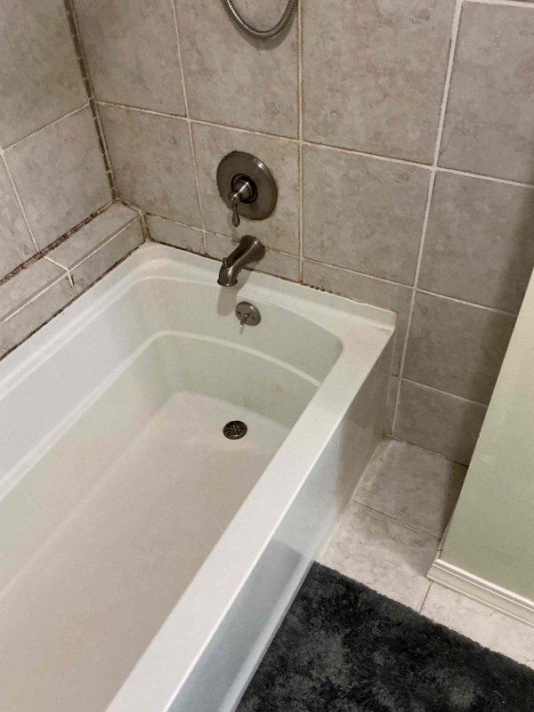 Responded to water leak complaint originating from master bathroom shower/tub area with visible damage to garage ceiling below. Upon inspection, identified deteriorated grout lines and caulking around tub-to-tile transition points showing significant discoloration and moisture infiltration. Observed compromised waterproofing at shower fixture penetrations and along bathtub perimeter where tile meets tub surface. Documented existing conditions with photographs showing aged grout, possible mildew presence, and darkened caulk joints indicating chronic water seepage. Due to extent of water damage and need for comprehensive moisture remediation in affected ceiling area, referred customer to restoration specialist for proper drying, mold assessment, and structural repair before plumbing repairs can be completed.
