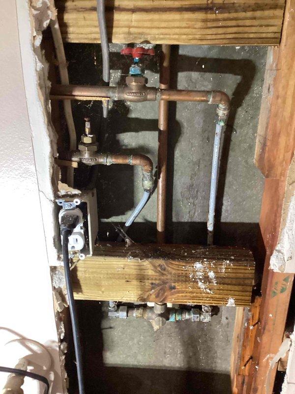 Responded to emergency water leak with main water supply shut off to property. Accessed wall cavity behind shower and identified failed polybutylene 3/8" supply line feeding shower valve as source of active leak. Removed section of drywall to expose plumbing infrastructure and assess extent of damage. Documented existing conditions showing deteriorated poly supply lines, aged copper piping with oxidation, and water staining on horizontal framing members. Provided estimates for two repair options: complete shower valve replacement with new supply lines, or replacement of supply lines only while retaining existing valve assembly.
