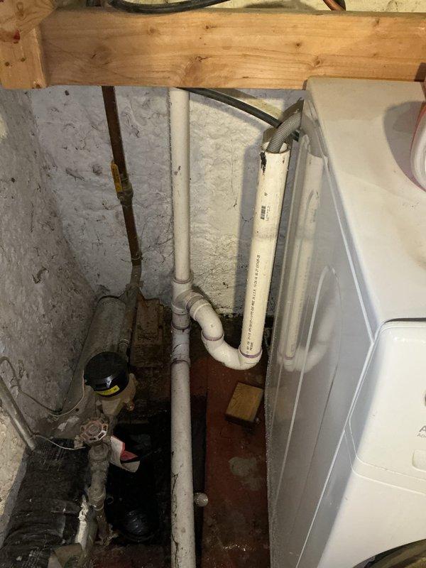 Responded to laundry drain backup causing standpipe overflow when washing machine discharged. Diagnosed blockage at point where drain enters ground, determined to be residual toilet paper from previous mainline obstruction. Cut drain line apart and extracted large accumulation of toilet paper debris. Cabled drain line to clear remaining blockage and restore proper flow. Installed repair band on laundry drain pipe to secure connection. Performed flow test by running water through system for approximately five minutes with no backup observed, confirming drain line fully opened and functioning properly.