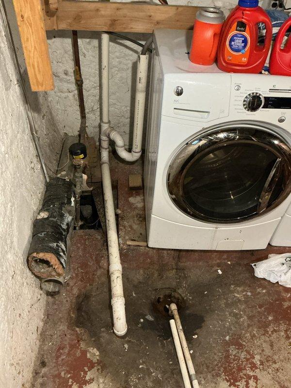 Responded to laundry drain backup causing standpipe overflow when washing machine discharged. Diagnosed blockage at point where drain enters ground, determined to be residual toilet paper from previous mainline obstruction. Cut drain line apart and extracted large accumulation of toilet paper debris. Cabled drain line to clear remaining blockage and restore proper flow. Installed repair band on laundry drain pipe to secure connection. Performed flow test by running water through system for approximately five minutes with no backup observed, confirming drain line fully opened and functioning properly.
