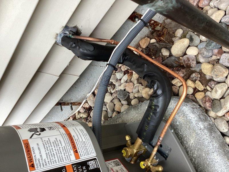 Responded to warranty call for noisy AC system with sound resonating inside residence. Replaced condensing unit as preventative measure, though original unit appeared to operate normally with standard sound levels at exterior location. Installed sound-deadening 90-degree elbows on refrigerant line set at outdoor installation point, which reduced interior noise resonance but did not fully resolve the issue. System remains operational but requires follow-up service to address persistent noise transmission into living space. Recommended solution involves installing new refrigerant line set routed through unfinished area to eliminate vibration transfer and sound resonance into occupied spaces.