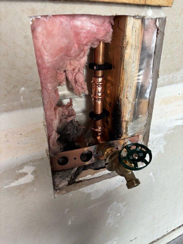 Responded to reports of a leaking outdoor spigot and water hammer in the plumbing system. Upon inspection, confirmed the exterior hose bib in the garage required replacement and that hydraulic shock was occurring when the dishwasher, washing machine, and faucets were shut off abruptly.

Performed drywall access work by cutting an opening in the garage wall to expose the copper supply lines and existing hose bib assembly. Removed the failed outdoor faucet and installed a new brass hose bib, securing all connections to copper piping. Restored water supply from the interior shutoff valve and pressure tested the new installation for leaks. Confirmed proper operation of the exterior faucet.

Addressed the water hammer issue by replacing the worn hammer arrestors at the washing machine connections. The old arrestors had lost their air cushion capacity, allowing pressure surges to create banging sounds throughout the plumbing system when water flow stopped suddenly. Installed new hammer arres