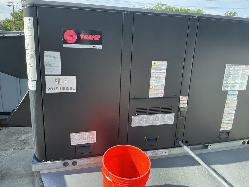 Responded to service call for commercial Trane rooftop unit RTU-6 with weak airflow complaint. Performed preventative maintenance inspection on 10+ year old unit, documented equipment condition with photographs showing multiple RTU installations on commercial facility rooftop. Unit operational at time of service with all safety labels and specifications visible and intact.