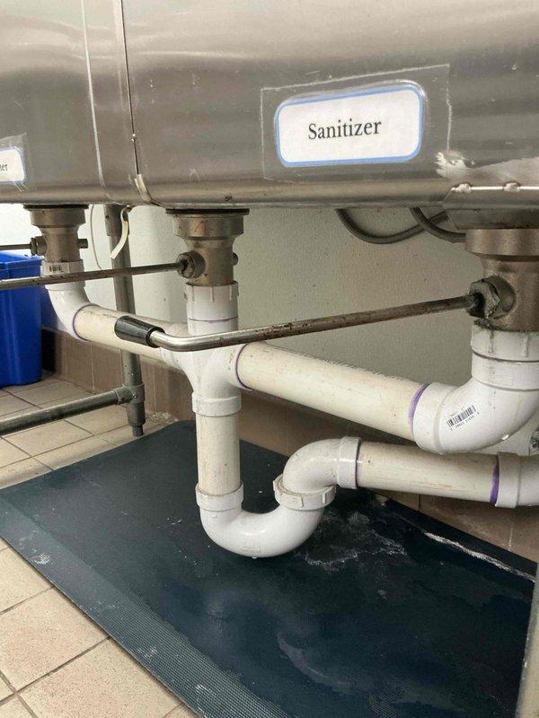 Assessed triple-basin commercial sanitizer sink with deteriorating drain basket strainers and gasket rings. Initial replacement parts were incompatible with existing fixtures. Documented existing plumbing configuration including PVC drainage system and sink drain assemblies. Provided bid for complete replacement of all three sink basket strainers with proper specifications.