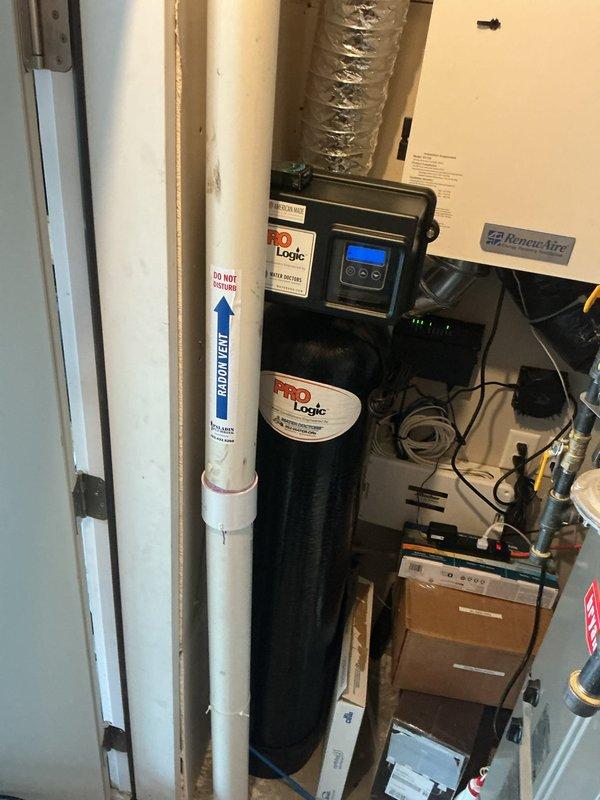 Responded to service call for leaking water heater in basement utility area. Upon inspection, found 50-gallon electric Rheem Classic series water heater with visible corrosion and active leak originating from bottom of tank. Unit was approximately 3 years old and showed signs of internal tank failure with rust-through condition. Documented existing installation including copper supply lines, brass fittings, flexible gas connections, and orange PEX distribution piping. Noted water softener system and Logic filtration equipment in immediate vicinity of failed heater. Assessed plumbing configuration including pressure gauge, wall-mounted connections, and hot water return line. Provided estimates for complete water heater replacement due to irreparable tank corrosion and leak severity.