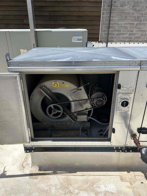 Responded to service call for kitchen make-up air unit producing excessive noise. Upon inspection, found supply fan motor running extremely hot to touch and generating loud operational sounds. During testing, motor failed to restart and interlock 2 tripped on control panel. Unable to cycle power to kitchen hood equipment as customer required continued use of cooking equipment during business hours. Temporarily adjusted hood system to maximum airflow to maintain adequate ventilation. Documented equipment condition with photographs of rooftop HVAC installation and internal blower assembly. Unit requires power reset to all kitchen hood equipment and motor replacement to restore proper operation.
