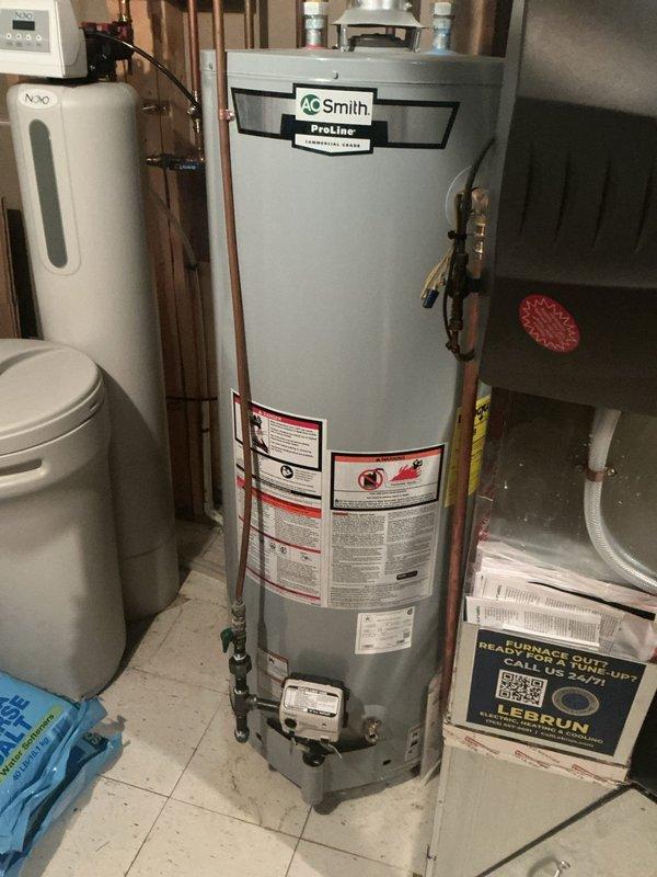 Responded to water leak emergency call for pinhole leak on copper supply line near water meter entry point in basement. Upon arrival, confirmed active leak on vertical copper pipe where main water line enters structure from ground. Leak was located on aged copper piping showing oxidation and patina, positioned adjacent to AO Smith ProLine water heater and water softening system. 

Performed repair of pinhole leak using appropriate copper pipe repair method. Applied white cloth wrapping at repair joints to secure connection points. Verified water meter shutoff valve was operational with red handle control. Tested repaired section under full water pressure to confirm leak was eliminated and no additional seepage was present at repair site or surrounding connections. Main water supply remained active throughout service as customer had not needed to shut off water to home prior to arrival.

Documented basement utility area configuration including proximity to water heater, filtration equip