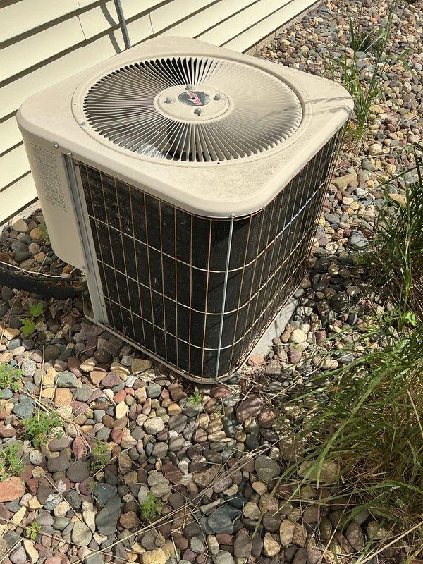Completed comprehensive air conditioning maintenance tune-up on a 25-year-old outdoor condensing unit as part of a recurring Family Rewards cooling visit. Upon inspection, discovered the system was low on R22 refrigerant, which was documented for the comfort advisor to address with the customer regarding options for this aging system. The unit, positioned on a gravel pad alongside the building with white vinyl siding, showed typical signs of weathering consistent with its age but remained operational throughout the service visit.