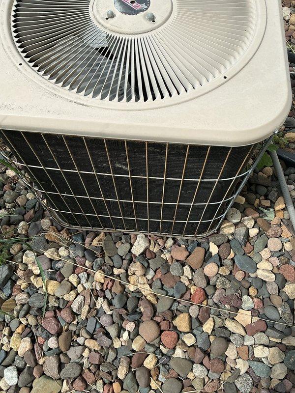 Completed comprehensive air conditioning maintenance tune-up on a 25-year-old outdoor condensing unit as part of a recurring Family Rewards cooling visit. Upon inspection, discovered the system was low on R22 refrigerant, which was documented for the comfort advisor to address with the customer regarding options for this aging system. The unit, positioned on a gravel pad alongside the building with white vinyl siding, showed typical signs of weathering consistent with its age but remained operational throughout the service visit.