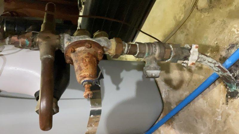 Responded to a water main leak at the residential property. Upon inspection, identified a slow drip originating from a corroded ball valve and coupling assembly located on the main water line prior to the water meter and main shut-off valve. The leak had been present for approximately two years. The plumbing infrastructure showed significant age-related deterioration, with extensive rust and corrosion visible on the brass valve body and copper pipe connections. Documented the condition of the aging plumbing system, including the corroded valve assembly and mixed materials from previous repairs. Explained that water service would need to be shut off from the exterior supply line to properly address the leak, as the affected components are positioned upstream of the interior shut-off valve. Provided the customer with multiple repair options to resolve the leak and prevent further deterioration of the water supply system.