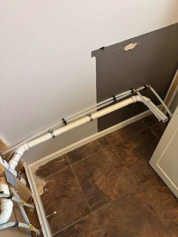 Completed rough-in plumbing installation for future laundry sink in utility room. Accessed powder room plumbing through shared wall to tap into existing drain and water lines. Installed 1-1/2" drain line connecting to powder room stack with proper venting tied into existing vent system. Added cleanouts to powder sink stack with arm cleanout extending into 24" deep cabinet for future access. Routed drain, waste, venting, and water supply lines through dead space behind cabinet locations to accommodate customer-supplied 18"x24"x10" drop-in utility sink and pull-down faucet. Installed blue-handled shut-off valves on water supply lines and secured all piping to wall framing with appropriate mounting brackets. Pressurized system and conducted leak test on all new connections with no leaks detected. All rough-in work positioned for final fixture installation after cabinetry and countertops are completed.