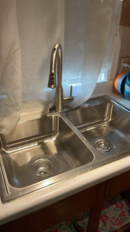 Replaced kitchen sink and faucet assembly due to leaking fixtures. Installed new stainless steel double-basin sink with modern single-lever faucet featuring pull-down spray head in brushed nickel finish. Replaced all drain piping underneath including P-traps and installed new hot and cold water shut-off valves to ensure proper water control and prevent future leaks.
