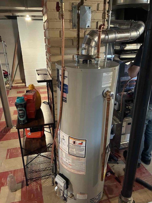 Installed a new 40-gallon Bradford White tanked water heater in the basement utility area. The installation included proper copper pipe connections to inlet and outlet ports, metallic vent pipe configuration with elbow joint for horizontal exhaust routing, and verification of all manufacturer specifications and safety requirements.