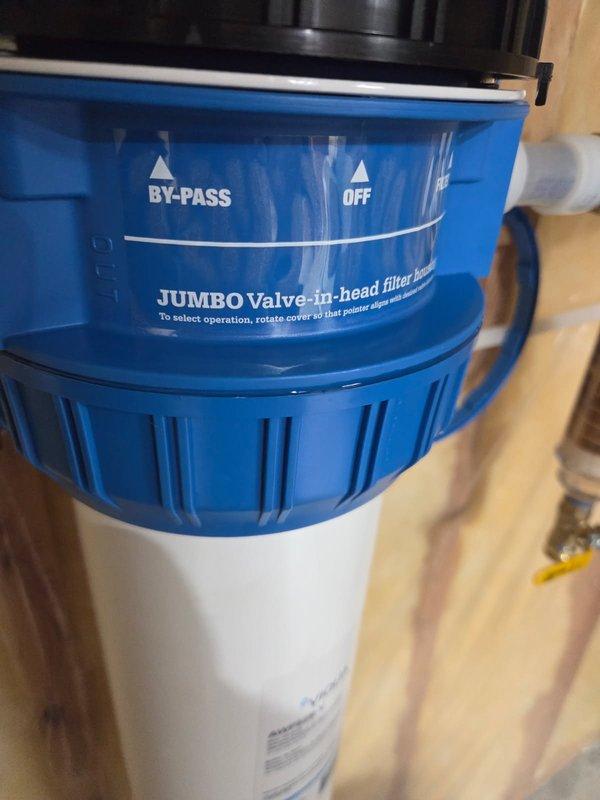 Responded to leak complaint on previously installed Jumbo Valve-in-head water filter housing system. Upon inspection, identified improper seal on filter canister causing water leakage. Removed and reinstalled filter housing unit, ensuring proper threading and O-ring seal between blue head assembly and white filter canister. Verified system operation through bypass, off, and filtration modes, confirming no active leaks and proper functionality upon completion.