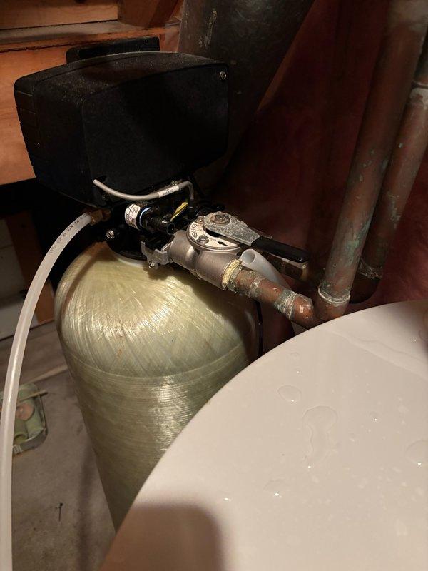 Responded to service call for water heater installed two weeks prior with no hot water and water pooling on top of unit. Upon inspection, discovered pilot light was extinguished and water softener discharge hose had disconnected, causing water to spray onto the water heater and extinguish the pilot. Removed damaged section of discharge pipe and reinstalled connection using hose clamp for additional security. Relit pilot light, which ignited successfully. Monitored unit for ten minutes to verify proper operation and sustained combustion. Water heater restored to full functionality with no further issues observed.