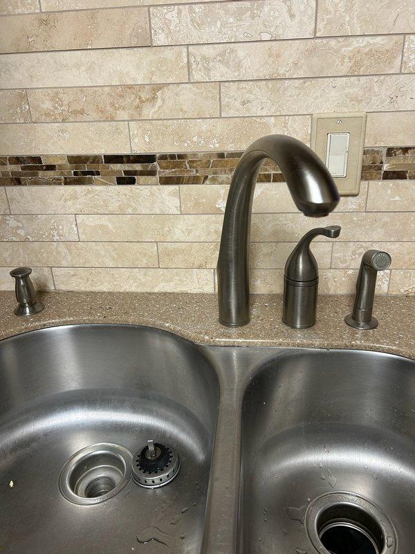 Responded to kitchen faucet leak complaint with water leaking onto countertop. Upon inspection, identified failed cartridge causing spout leak in existing bronze finish faucet assembly. Removed and replaced entire faucet system with new Moen three-piece fixture set including high-arc spout, side spray attachment, and soap dispenser component in coordinating oil-rubbed bronze finish to match existing décor. Installed on double-basin stainless steel sink with granite countertop. Tested all components for proper operation and verified leak resolution with no water discharge onto counter surface.
