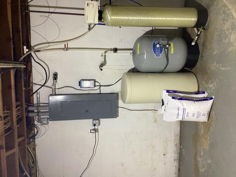 Completed comprehensive plumbing inspection of residential property, examining water treatment system components including three-stage filtration tanks with control valves and electrical connections, as well as sump pump basin and drainage infrastructure. Conducted visual assessment of all accessible plumbing systems, copper piping, and utility connections to verify proper operation and identify any maintenance concerns.