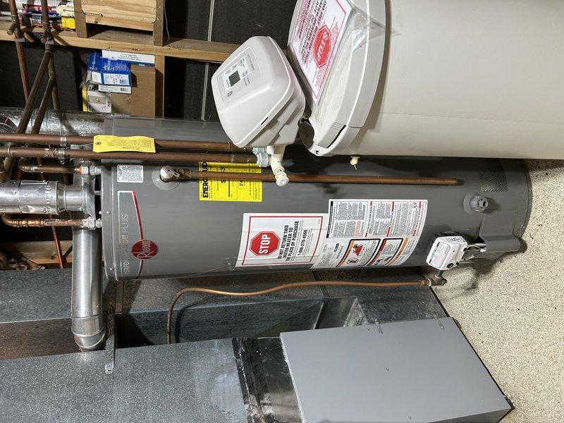 Responded to recurring water leak in basement originating from utility room area. Upon inspection, identified hot water supply valve for washing machine connection in open position with no appliance attached, causing water to spray into basement when pressurized. Shut off disconnected hot side washer valve to stop active leak and prevent further water damage. Documented water heater installation and affected utility room area with photographs for service records.