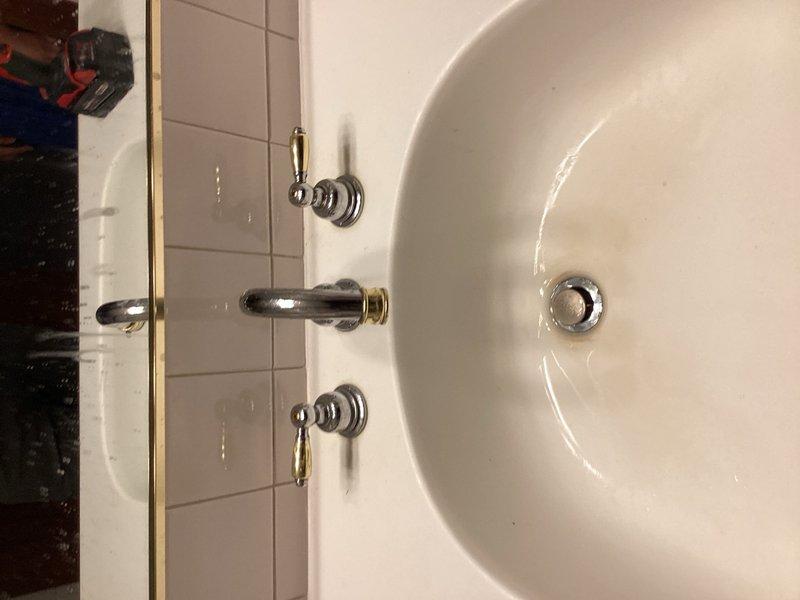Conducted comprehensive plumbing assessment of bathroom fixtures including wall-mounted faucet assembly with separate hot and cold water control valves and toilet tank components. Documented existing conditions of chrome and brass-toned fixtures, identified mineral buildup on internal tank mechanisms, and photographed current state of installations for estimate preparation.