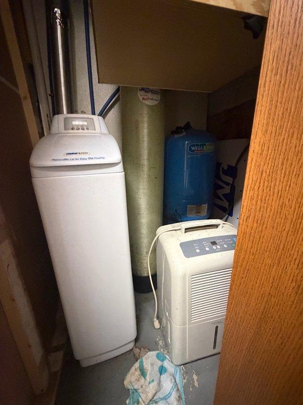 Responded to emergency call for active water heater leak causing water damage to surrounding floor area. Upon inspection, identified leak originating from bottom jacket of existing tanked water heater, indicating tank failure and requiring immediate replacement. Removed failed water heater unit and installed new tanked water heater in utility closet alongside existing water treatment equipment including water softener and well pressure tank system. Connected all supply and discharge plumbing lines, verified proper venting through existing metallic duct system, and tested unit operation to ensure proper heating function and confirmed no leaks at connections. Placed dehumidifier in area to assist with drying from previous water damage.