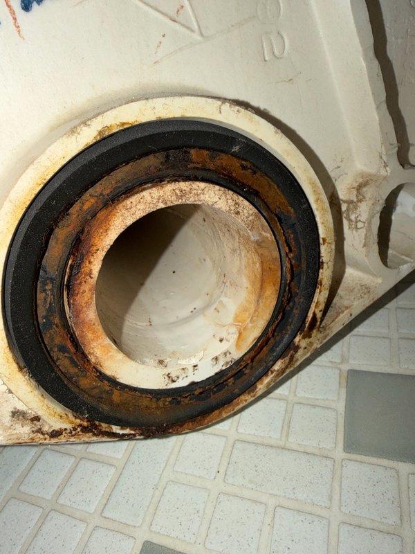 Responded to water leak complaint manifesting as ceiling stain on first floor below guest bathroom. Upon inspection, no visible water damage observed in guest bathroom itself. Removed wall-mounted toilet to access and inspect wax ring seal and flange connection. Inspection revealed corroded toilet flange with rust accumulation and deteriorated sealing components requiring replacement. Temporarily reset toilet to maintain facility function while awaiting replacement parts. Opened access point in plaster ceiling below to monitor for active leakage and verify source of water intrusion. Confirmed leak originated from compromised toilet seal at flange connection. Documented extensive corrosion on metal flange components and gasket deterioration through photographic evidence. Return visit scheduled to install new flange seal, permanently reset wall-mounted toilet, and repair plaster ceiling access opening upon parts arrival.