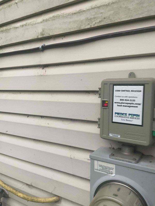 Responded to no-cooling complaint on 8-12 SEER AC system installed within past year. Diagnosed issue as load control receiver (energy saver box) from electric utility preventing unit operation. Bypassed load control device to restore immediate cooling functionality. Customer advised to contact Pierce Cooperative Services electrical company regarding load control receiver interference with AC operation.