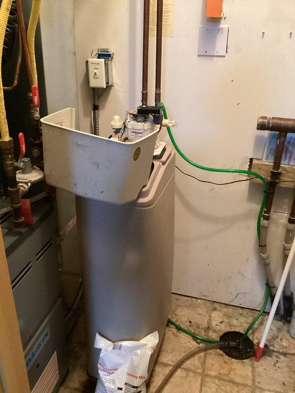 Responded to call for leaking water softener system. Upon inspection, found 20-year-old water softener actively leaking from top of unit and continuously filling. Identified that system lacked dedicated shut-off valve for isolation. Determined unit had reached end of serviceable life and required full replacement. Documented existing plumbing configuration including copper supply lines and connections to main water distribution system. Advised replacement of entire water softener unit due to age and condition of equipment.