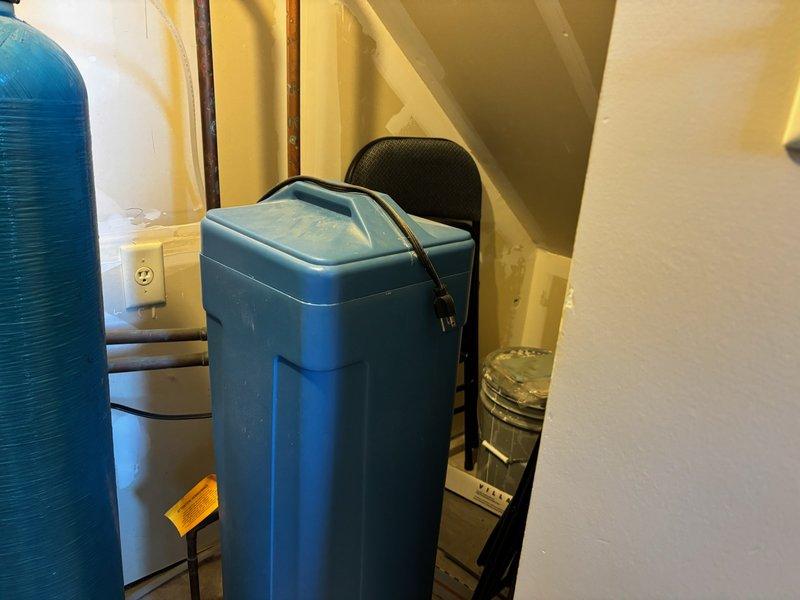 Responded to a water softener leak complaint at a townhome with an approximately 20-year-old water treatment system. Upon inspection, identified a slight leak on the existing teal-colored cylindrical water softener unit with digital control valve head. Assessed the condition of the aging system, including the pressure tank and associated copper piping connections. Documented the equipment configuration and leak source through photographic documentation for maintenance records and future service recommendations.