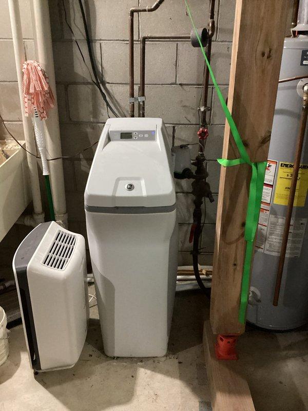 Replaced non-functional 15-year-old water softener system with new unit in basement utility area. The existing softener had ceased operation and was beyond economical repair, requiring complete replacement. Installed new water treatment system with digital control panel, connected to existing copper supply lines and drain plumbing, and verified proper operation of all functions.