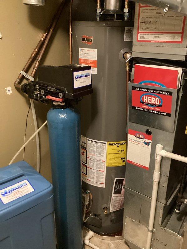 Responded to callback for water heater leaking from bottom of tank following recent installation. Upon inspection, confirmed active leak at base of RUUD residential water heater with water accumulating in catch pan. Documented leak location with photos showing moisture on copper connections and tank surface. Determined tank failure requiring complete water heater replacement to resolve issue.