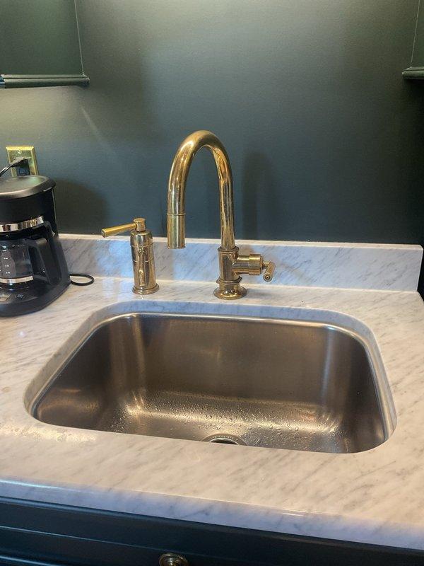 Returned to complete kitchen faucet installation that was previously unable to be finished due to a seized set screw. Successfully removed the problematic set screw and installed new gold-finish high-arc faucet with side spray attachment on undermount stainless steel sink. All components tested and functioning properly upon completion.