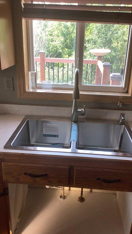 Completed installation of customer-supplied dual-basin stainless steel kitchen sink and contemporary pull-down faucet in existing wooden countertop. Secured sink mounting, connected hot and cold water supply lines to shut-off valves, installed faucet assembly with sprayer head, and tested all connections for proper operation and leak-free performance.