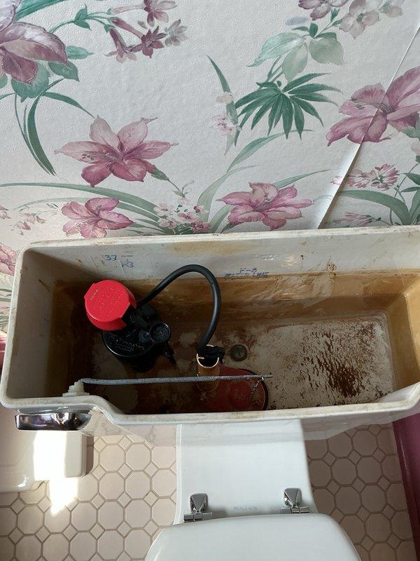 Responded to upstairs toilet leaking into ceiling below. Removed toilet to diagnose issue and found cast-iron repair flange loose and rocking excessively. Secured and tightened repair flange to cast-iron drain to ensure stable connection. Reset toilet with proper shimming to achieve level installation and prevent future movement. Performed multiple flush tests to verify watertight seal. Additionally replaced deteriorated fill valve to restore proper tank function.