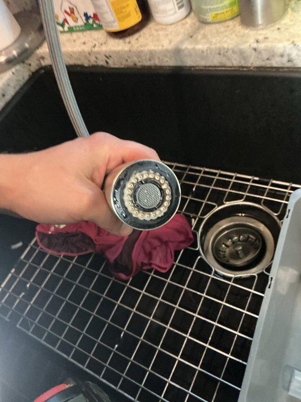 Responded to complaint of squealing noise from kitchen faucet and dishwasher that began after water heater replacement. Inspected Moen kitchen faucet and identified significant hard water deposits on faucet head and aerator. Confirmed squealing noise ceased when faucet head was removed, indicating mineral buildup as root cause. Recommended vinegar soak treatment for existing faucet head to dissolve calcium deposits, with replacement head as alternative solution if cleaning proves ineffective. Advised installation of water softening system to prevent future mineral accumulation throughout plumbing fixtures.