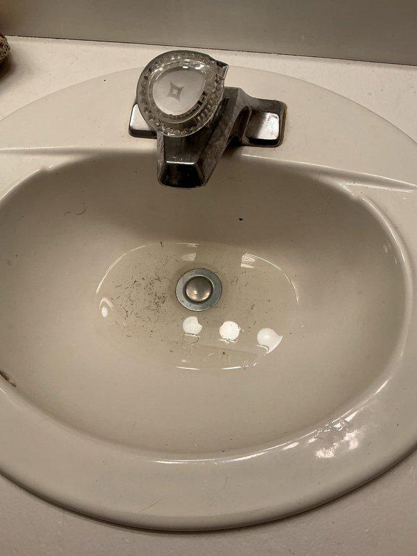 Responded to a bathroom vanity sink with a stuck pop-up drain stopper. Upon diagnostic inspection, determined that the trip lever assembly had become disconnected, allowing the stopper mechanism to lodge in the drain and prevent proper drainage. Removed the P-trap to gain access to the stopper from below and used a screwdriver to push the stopper upward through the drain opening for extraction. Reassembled the trip lever linkage and secured it with a rubber band behind the connection point to prevent future disconnection. Reinstalled the P-trap and tested the pop-up stopper assembly for proper operation. Verified full range of motion for opening and closing the drain stopper and confirmed no leaks at trap connections. System restored to full functionality.