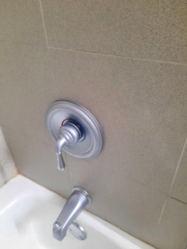 Installed customer-supplied shower trim kit in bathroom with beige speckled tile surround. Completed installation of chrome single-handle shower valve control with circular escutcheon plate and matching chrome tub spout below, both fixtures mounted on tiled wall above existing bathtub. All components secured properly and tested for functionality, with polished chrome finish ensuring consistent appearance throughout the installation.