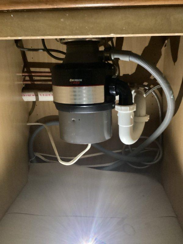 Removed end-of-life garbage disposal unit and associated mounting hardware from kitchen sink drain system. Installed new sink strainer basket in disposal opening and reconfigured drain plumbing with white PVC P-trap assembly to establish proper drainage without disposal unit. Tested all connections for leaks and verified proper drain flow upon completion.