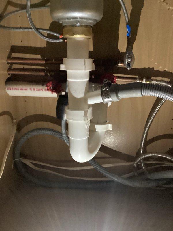 Removed end-of-life garbage disposal unit and associated mounting hardware from kitchen sink drain system. Installed new sink strainer basket in disposal opening and reconfigured drain plumbing with white PVC P-trap assembly to establish proper drainage without disposal unit. Tested all connections for leaks and verified proper drain flow upon completion.