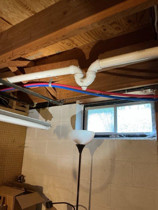Responded to complaint of gurgling noises from toilet when shower was in use in basement bathroom. Upon inspection, identified improper venting throughout the plumbing system resulting from previous remodeling work. Examined exposed plumbing infrastructure in ceiling area, including PVC drain lines and vent piping configuration. Determined that drain-waste-vent system was not installed to code specifications, causing negative air pressure and gurgling sounds during fixture use. Documented existing conditions with photographs showing inadequate venting arrangement and improper trap configuration. Recommended complete re-piping and proper venting installation to resolve drainage issues and bring system up to code compliance.