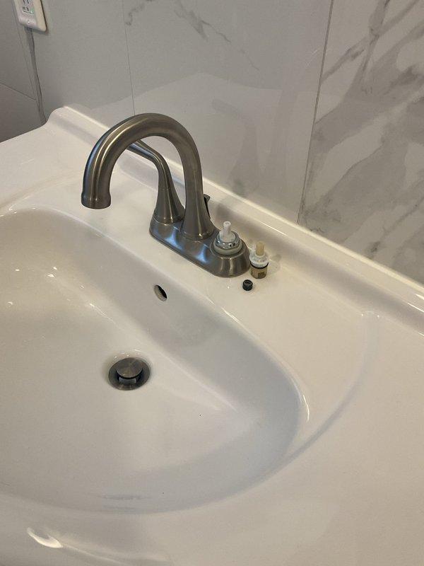 Completed labor-only installation of customer-supplied bathroom faucet assembly on white ceramic countertop sink. Installed dual-handle brushed nickel faucet with high-arc spout, including valve cartridges, mounting hardware, and drain assembly components. Tested system for proper operation and verified no leaks upon completion.