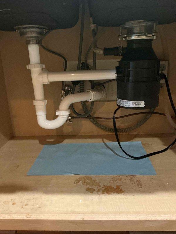 Completed kitchen sink reinstallation following countertop installation. Connected double bowl sink with owner-supplied components including garbage disposal, strainers, continuous waste assembly, and P-trap. Installed disposal unit with proper electrical connection and mounting hardware, configured drain assemblies for both sink basins, and reconnected dishwasher drain line to disposal. All plumbing connections tested and verified leak-free with proper drainage function.
